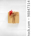 Gift box of craft paper with red flowers on the white wooden background. Valentine's Day. Happy birthday. 98847314