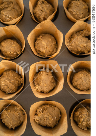 Scooping dough with dough scoop into cupcake pan lined with tulip paper muffin liners to bake banana oatmeal muffins. Scooping dough with dough scoop into cupcake pan lined with tulip paper muffin liners to bake banana oatmeal muffins. 98847686