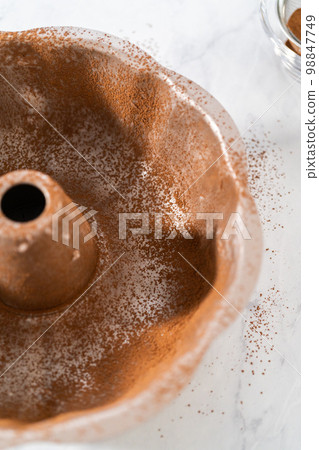 Greasing metal bundt cake pan with vegetable shortening and cocoa powder to bake gingerbread bundt cake with caramel filling. 98847749