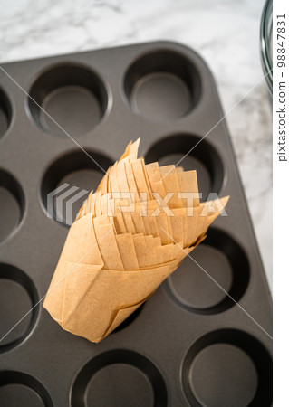 Scooping dough with dough scoop into cupcake pan lined with tulip paper muffin liners to bake banana oatmeal muffins. Scooping dough with dough scoop into cupcake pan lined with tulip paper muffin liners to bake banana oatmeal muffins. 98847831