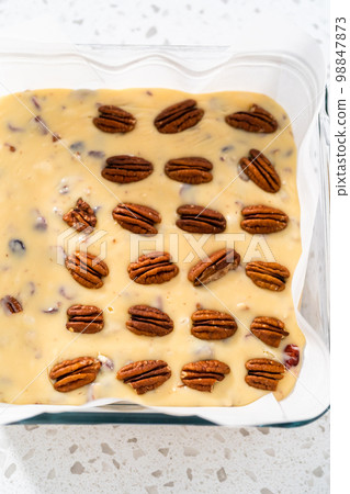 Pouring fudge mixture into the baking pan lined with parchment paper to prepare white chocolate cranberry pecan fudge. 98847873