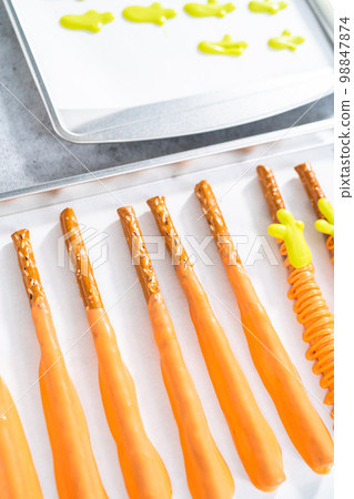 Dipped in chocolate pretzel rods on a baking sheet with parchment paper. 98847874