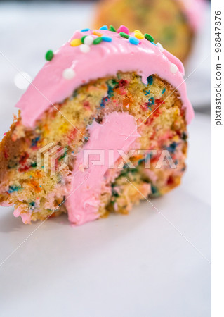 Close up view. Sliced funfettti bundt cake with pink buttercream frosting on top and buttercream filling inside. Close up view. Sliced funfettti bundt cake with pink buttercream frosting on top and buttercream filling inside. 98847876