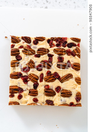 Cutting white chocolate cranberry pecan fudge into small pieces on a white cutting board. 98847908