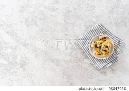 Flat lay. Homemade cranberry pistachio fudge square pieces on a white plate. Flat lay. Homemade cranberry pistachio fudge square pieces on a white plate. 98847938