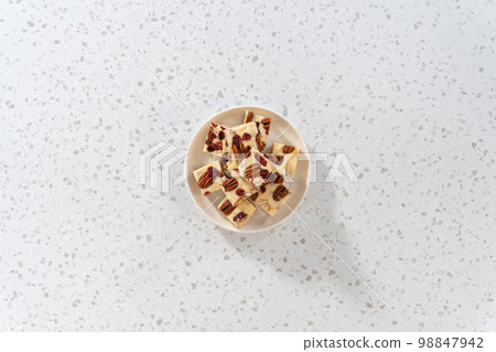 Flat lay. Homemade white chocolate cranberry pecan fudge pieces on a white ceramic plate. Flat lay. Homemade white chocolate cranberry pecan fudge pieces on a white ceramic plate. 98847942