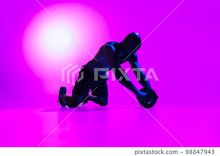 Bodybuilder working on his abs with a ab roller on studio background with color filter Bodybuilder working on his abs with a ab roller on studio background with color filter 98847943