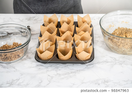 Scooping dough with dough scoop into cupcake pan lined with tulip paper muffin liners to bake banana oatmeal muffins. 98847963