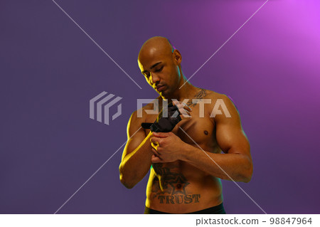 Portrait of muscular man puts on fighting gloves posing on studio background with color filter Portrait of muscular man puts on fighting gloves posing on studio background with color filter 98847964