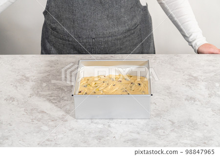 Filling square cheesecake pan lined with parchment paper with fudge mixture to prepare cranberry pistachio fudge. 98847965