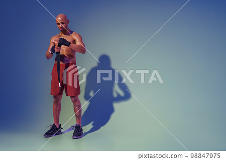 Sporty man with naked torso taping his arms with bandage before fight on studio background 98847975