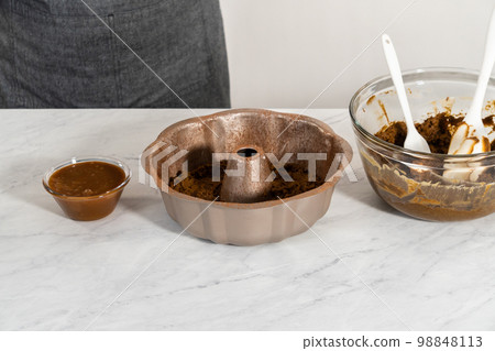 Filling metal bundt cake pan with cake butter to bake gingerbread bundt cake with caramel filling. 98848113