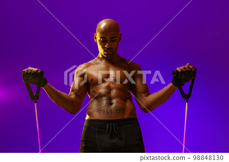Sporty man performs exercises with expander on violet studio background. Strength and motivation Sporty man performs exercises with expander on violet studio background. Strength and motivation 98848130