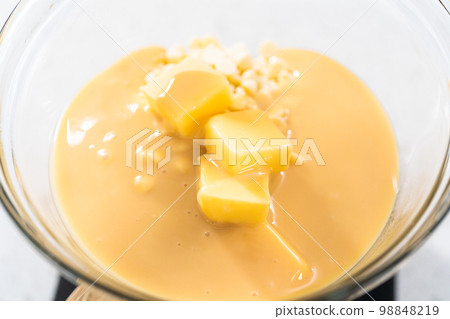 Melting white chocolate chips and other ingredients in a glass mixing bowl over boiling water to prepare white chocolate cranberry pecan fudge. 98848219