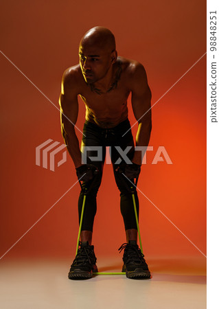 Sporty man performs exercises with expander on studio background. Strength and motivation Sporty man performs exercises with expander on studio background. Strength and motivation 98848251