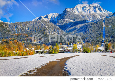 Road in alpine woodland and snowy pine woods in bavarian Alps at autumn, Germany 98849780