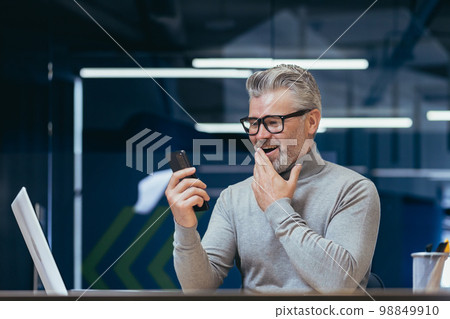 Mature businessman with beard using app on phone inside office, man received online message notification about good news, boss texting online at workplace. 98849910