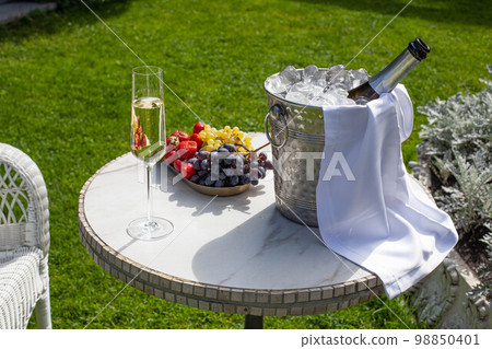 Champagne glass with sparkling wine and bottle in bucket with ice near fruits Champagne glass with sparkling wine and bottle in bucket with ice near fruits 98850401
