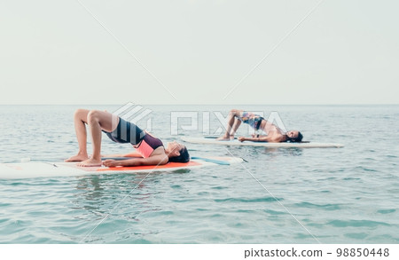 Woman sup yoga. Happy young sporty woman practising yoga pilates on paddle sup surfboard. Female stretching doing workout on sea water. Modern individual female outdoor summer sport activity. Woman sup yoga. Happy young sporty woman practising yoga pilates on paddle sup surfboard. Female stretching doing workout on sea water. Modern individual female outdoor summer sport activity. 98850448