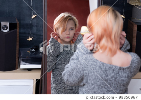teenager girl looks in the mirror in the studio, carefully examines her hairstyle 98850967