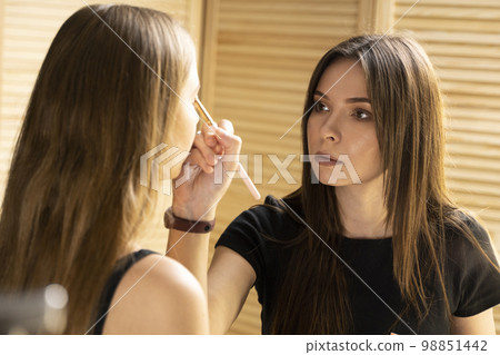 Makeup artist applies a make up on a model face, painting cosmetics of young beauty model girl. Make up in process. Makeup artist applies a make up on a model face, painting cosmetics of young beauty model girl. Make up in process. 98851442