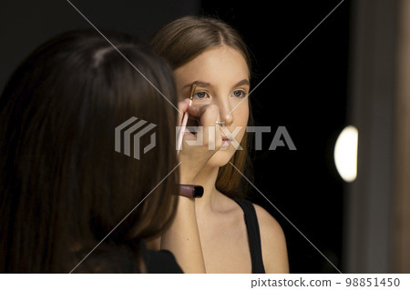 Close up makeup artist applies a make up on a model face. Beautiful woman with make-up face. Hand of visagiste, painting cosmetics of young beauty model girl. Close up makeup artist applies a make up on a model face. Beautiful woman with make-up face. Hand of visagiste, painting cosmetics of young beauty model girl. 98851450