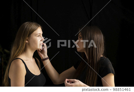 Makeup artist applies a make up on a model face. Beautiful woman with make-up face. Hand of visagiste, painting cosmetics of young beauty model girl. Make up in process. Makeup artist applies a make up on a model face. Beautiful woman with make-up face. Hand of visagiste, painting cosmetics of young beauty model girl. Make up in process. 98851461