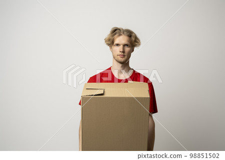 Young delivery man in red t-shirt standing with parcel post box isolated over white background. 98851502