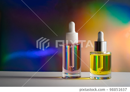 Yellow and pink face oil with a dropper bottle in rainbow prism light. Side view 98851637