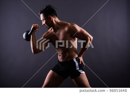 Sporty man working out with a kettlebell. Photo of man on dark background. Strength and motivation Sporty man working out with a kettlebell. Photo of man on dark background. Strength and motivation 98851648