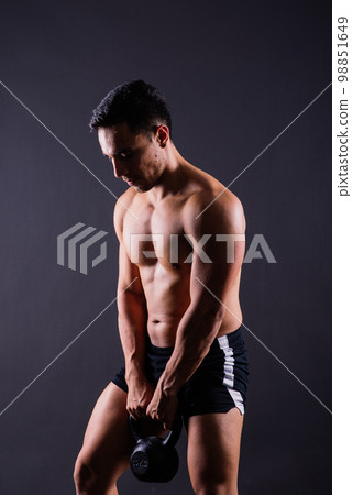 Sporty man working out with a kettlebell. Photo of man on dark background. Strength and motivation Sporty man working out with a kettlebell. Photo of man on dark background. Strength and motivation 98851649