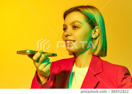 Half-length portrait of young emotional girl with blonde hair wearing red jacket using phone over yellow background. Concept of youth, student college life, business and education Half-length portrait of young emotional girl with blonde hair wearing red jacket using phone over yellow background. Concept of youth, student college life, business and education 98852822
