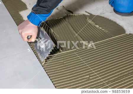 Tiler worker placing or tiling gray ceramic tile in the position over adhesive glue with lash tile leveling system, renovation or recontruction, concept of building 98853659