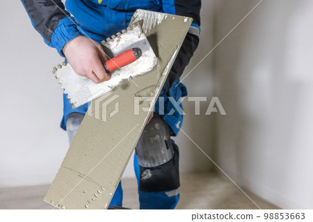 Tiler worker placing or tiling gray ceramic tile in the position over adhesive glue with lash tile leveling system, renovation or recontruction, concept of building 98853663
