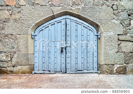 Blue wooden gate on wall surrounded by stones in medieval design hide mysterious things from arriving visitors. Exterior of medieval place 98856903