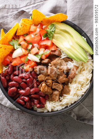 Chifrijo is a unique Costa Rican dish made by layering the following components rice, beans, chicharron pork, pico de gallo and tortilla chips closeup. Vertical top view 98859572