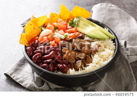 Costa Rican chifrijo is a layered dish of tender beans topped with chicharron and chimichurri served with tortilla chips closeup on the plate. Horizontal 98859575