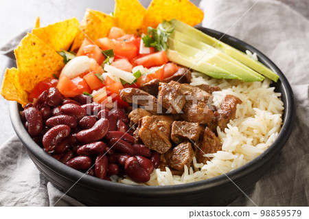 Chifrijo is a Costa Rican dish consisting mainly of stewed beans, white rice, pork chicharron and pico de gallo closeup on the plate. Horizontal 98859579