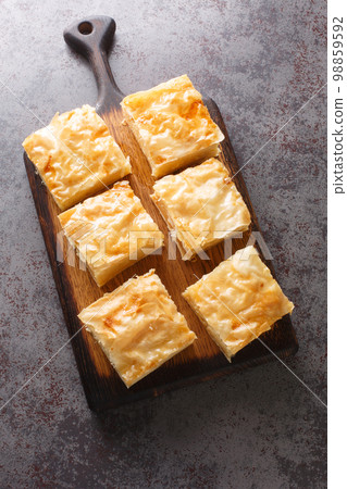 Galaktoboureko is a traditional Greek dessert featuring a custard in a crispy phyllo pastry closeup on the wooden board. Vertical top view Galaktoboureko is a traditional Greek dessert featuring a custard in a crispy phyllo pastry closeup on the wooden board. Vertical top view 98859592
