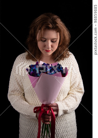 Attractive young woman smiling looking at a bouquet of orchids and roses against a black background. 98859885