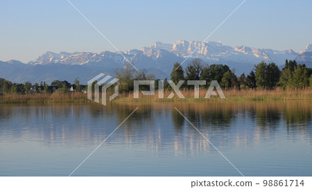 Shore of Lake Pfaffikon and snow capped mountains. 98861714