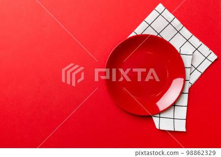 Top view on colored background empty round red plate on tablecloth for food. Empty dish on napkin with space for your design 98862329