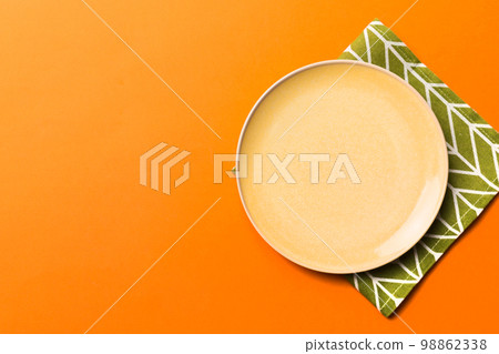 Top view on colored background empty round yellow plate on tablecloth for food. Empty dish on napkin with space for your design Top view on colored background empty round yellow plate on tablecloth for food. Empty dish on napkin with space for your design 98862338