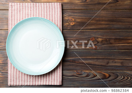 Top view on colored background empty round blue plate on tablecloth for food. Empty dish on napkin with space for your design Top view on colored background empty round blue plate on tablecloth for food. Empty dish on napkin with space for your design 98862384