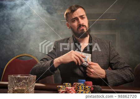 Handsome bearded man is playing poker sitting at the table in casino. 98862720