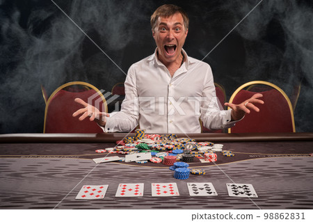 Handsome emotional man is playing poker sitting at the table in casino. 98862831