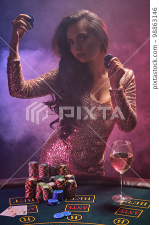 Brunette girl with a perfect hairstyle and bright make-up is posing with gambling chips in her hands. Casino, poker. 98863146