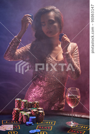 Brunette girl with a perfect hairstyle and bright make-up is posing with gambling chips in her hands. Casino, poker. 98863147