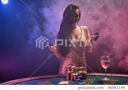 Brunette girl with a perfect hairstyle and bright make-up is posing with gambling chips in her hands. Casino, poker. 98863149