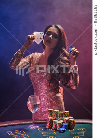 Brunette girl with a perfect hairstyle and bright make-up is posing with playing cards and chips in her hands. Casino, poker. 98863165
